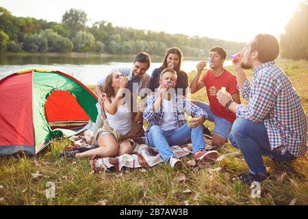 Young people make soap bubbles while sitting on the grass on in nature. Stock Photo