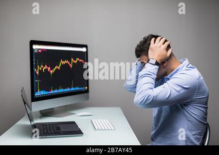 Man lamenting with hands on the head in front of computer with graph of unsuccessful business on the screen. Stock Photo