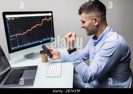 Businessmen trading stocks online. Stock brokers looking at graphs, indexes and numbers on multiple computer screens. Colleagues in discussion in trad Stock Photo