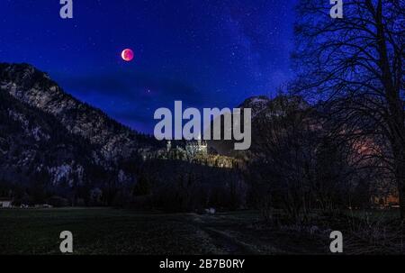Bloody moon over a castle with mountains in background in germany at the night sky. Stock Photo
