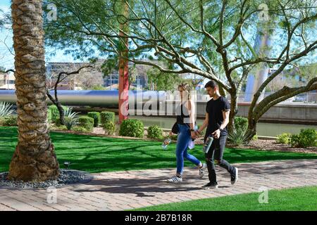 Young couple on walkway around the AZ canal waterfront across from the Paolo Soleri Bridge and plaza attractions in Scottsdale, AZ, USA Stock Photo
