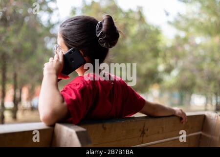 Young attractive woman talking through the phone and smiling in a park, sit down in a bench Stock Photo