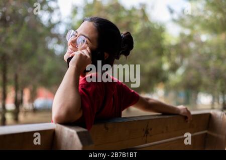 Young attractive woman talking through the phone and smiling in a park, sit down in a bench Stock Photo