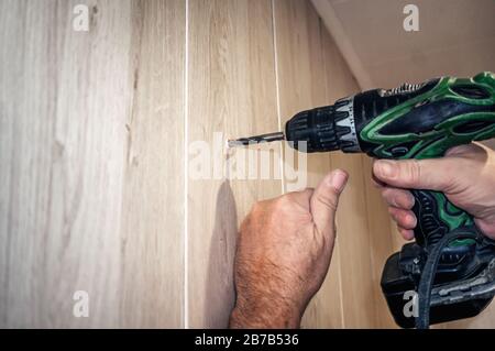 An electric drill makes a hole in a sheet of plywood. Authentic home renovation. Space for copying. Stock Photo