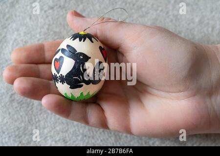 An decorated easter egg is kept in the palm of your hand. The egg is decorated with figures cut out of paper: bunny, egg, heart, flower, grass Stock Photo