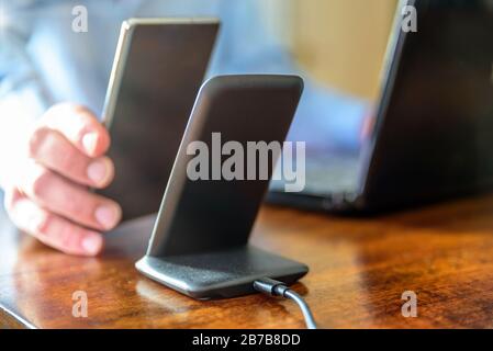 man charging smartphone using Wireless charging stand at home office Stock Photo