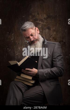 Portrait of a gray-haired bearded man with glasses reading book in Russian, on the cover Russian inscription M. Gorky, selective focus Stock Photo