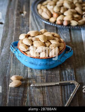 Almonds in a blue bowl on wooden table. Nut cracker tool. Health benefits, nutrition concept. Stock Photo