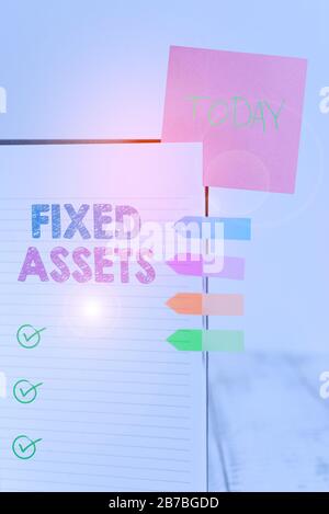 Writing note showing Fixed Assets. Business concept for longterm tangible piece of property or equipment a firm owns Hard cover note book sticky note Stock Photo