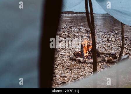Fire burning in fire pit next to tent and river on camping trip Stock Photo