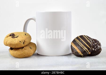 This coffee cup mockup features a white 11 oz. coffee mug resting on a gray marble background surrounded by chocolate chip and chocolate cookies. Stock Photo