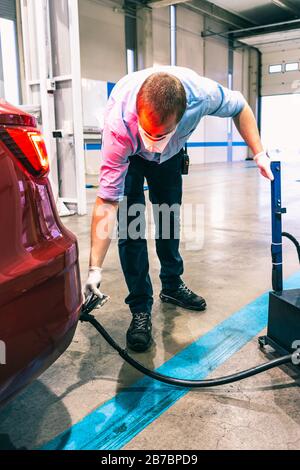 A young caucasian technician doing an emission control in a security inspection of a vehicle protected with a mask and gloves to prevent the spread of Stock Photo