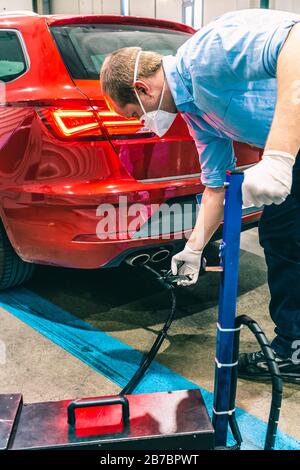 A young caucasian technician doing an emission control in a security inspection of a vehicle protected with a mask and gloves to prevent the spread of Stock Photo