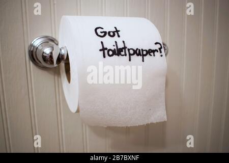 'Got Toilet Paper?' written on toilet paper roll with sharpie as it hangs on the wall on a silver spool. Stock Photo