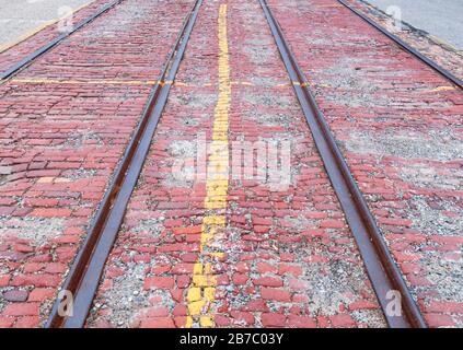 An old, worn red brick road showing trolley tracks that are no longer in use with gravel on parts of the bricks Stock Photo