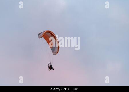 Powered paragliding, man flying high in a sky with parachute and engine on his back. The pink sky on a background, sunset. Stock Photo