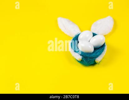 Easter eggs in a blue nest with bunny ears on a yellow background. Minimal concept Easter. Copy Space for text Stock Photo