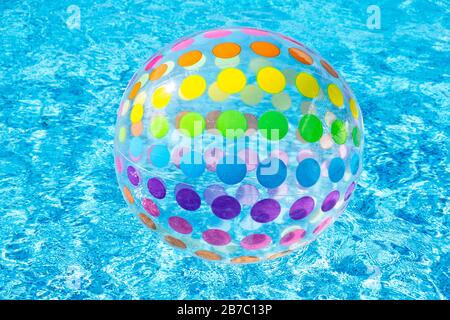 Inflatable colorful dotty Beach Ball Floating On Surface Of Swimming Pool blue water Stock Photo