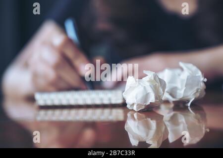 Closeup image of a businesswoman working and writing down on a white blank notebook with screwed up papers on table Stock Photo