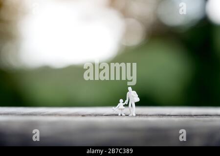 Closeup image of miniature figure model of father and daughter walking together on wooden table with blur background Stock Photo