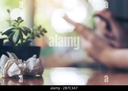 Closeup image of screwed up papers on table with a businesswoman working and writing down on a white blank notebook Stock Photo