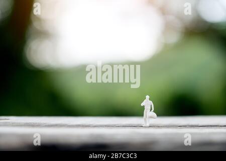 Closeup image of miniature figure model of a male traveler holding bag and standing on wooden table with blur background Stock Photo