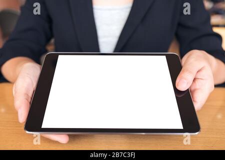 Mockup image of businesswoman holding and showing a black tablet pc with blank white desktop screen on table Stock Photo