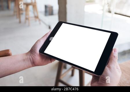 Mockup image of hands holding black tablet pc with blank white desktop screen on wooden table Stock Photo