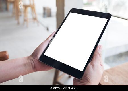 Mockup image of hands holding black tablet pc with blank white desktop screen on wooden table Stock Photo