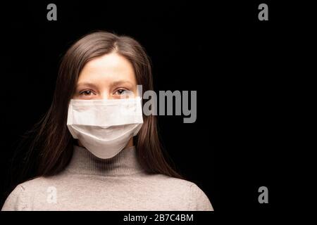 a woman's face in a mask , an outbreak of coronavirus infection and protection from it. close- up, Studio portrait on a dark background. copyspace, lo Stock Photo