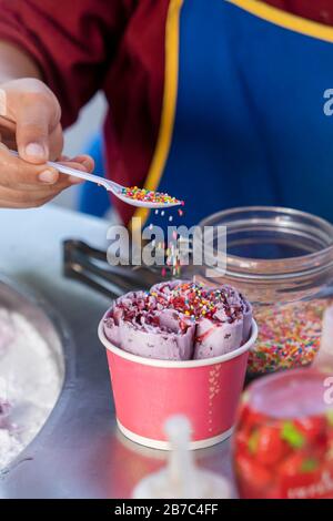 the preparation of ice-cream , Thai street food, cook sprinkles ice cream in a paper Cup with caramel. Vertival photo. Stock Photo