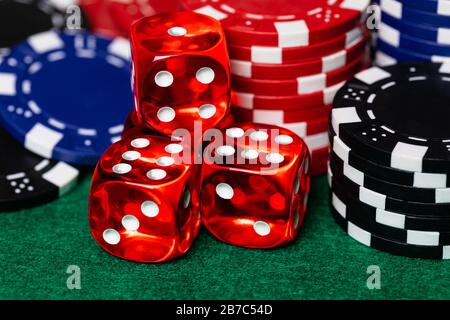 a macro of Red translucent casino style dice with white pips surrounded by reb, blue and black betting chips on a green felt gaming surface. High deta Stock Photo