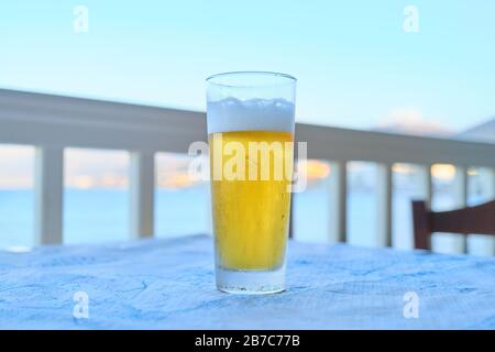 One glass of light beer on table in resort cafe, sea sunset background Stock Photo