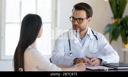 Doctor in eyeglasses listening to patient during checkup at clinic Stock Photo