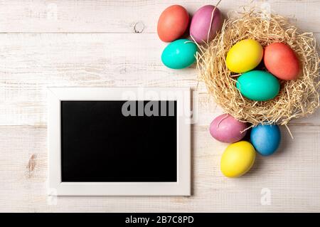 Easter concept. Colorful eggs on white wooden background with empty chalkboard. Copy space for greetings, text or design. Top down view or flat lay Stock Photo