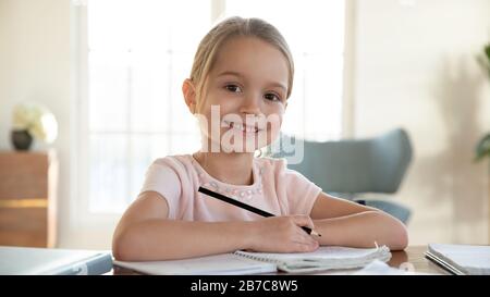 Smiling little child girl enjoying doing lessons at home. Stock Photo