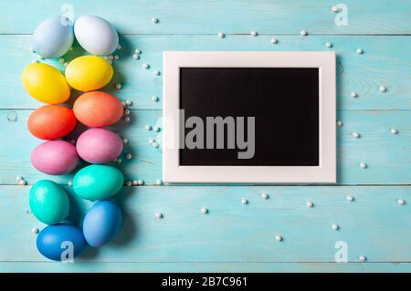 Easter concept. Colorful eggs on blue wooden background with empty chalkboard. Copy space for greetings, text or design. Top down view or flat lay Stock Photo