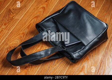 Black notebook peeking out of the pocket of a black leather bag close-up, macro Handmade, natural materials. Stock Photo
