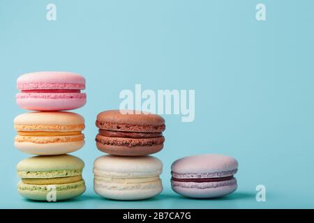 Macaroni cookies of different colors are arranged in the shape of pyramid steps on a blue background. Stock Photo