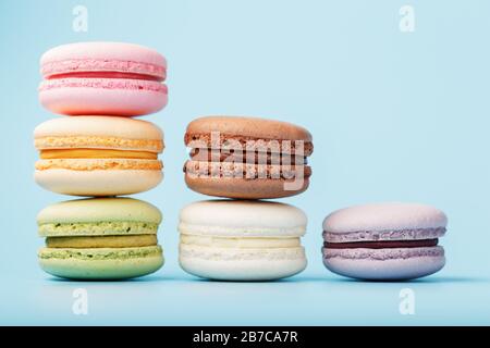 Macaroni cookies of different colors are arranged in the shape of pyramid steps on a blue background.