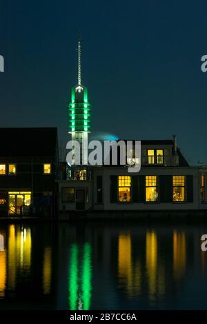 Classic dutch houses along the river Rhine in the town of Alphen aan den Rijn, Netherlands. Illuminated communication tower in the background. Stock Photo