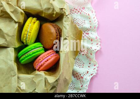 Yellow, pink, green and brown macaroons in the craft pack on pinc background Stock Photo
