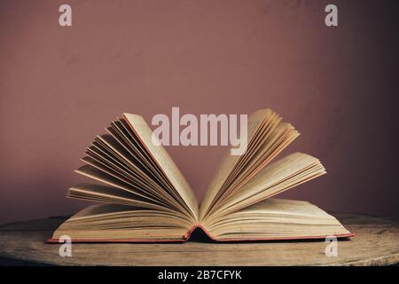 Open vintage ancient book. Pattern background for design. The book on a round wooden table and red wall background. Stock Photo