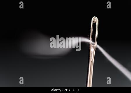 Needle with white thread threaded on black background Stock Photo