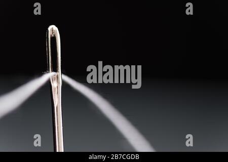 Needle with white thread threaded on black background Stock Photo