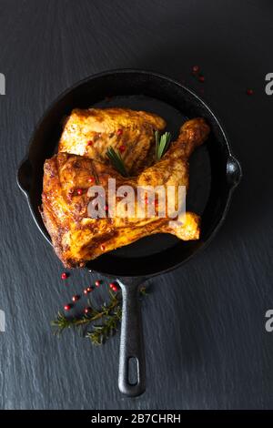 Food concept organic roasted or grilled chicken leg quarters in skillet iron pan on black slate stone plate Stock Photo