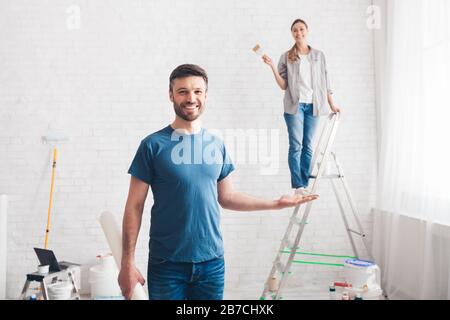 Man holding wife on palm while she painting walls Stock Photo