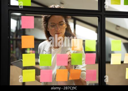 Confident businesswoman wearing glasses writing on sticky papers Stock Photo