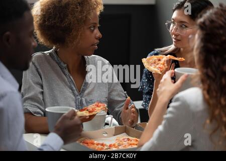 Diverse colleagues enjoying pizza together, chatting during lunch break Stock Photo