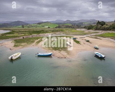 Small fishing boats at low tide on the Escudo river and the surrounding marsh land, in San Vicente de la Barquera, Cantabria, Spain Stock Photo